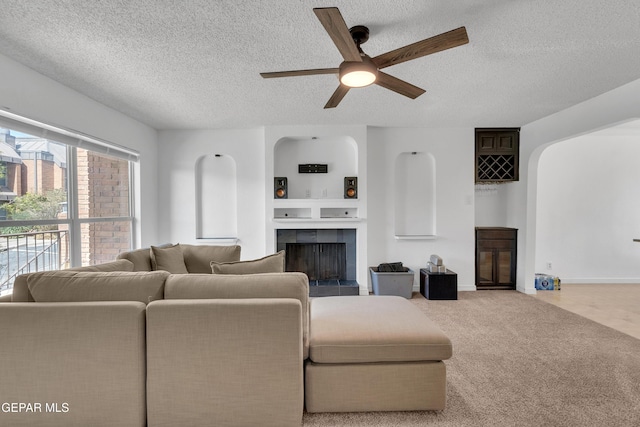 living area featuring a textured ceiling, a fireplace, carpet flooring, a ceiling fan, and baseboards