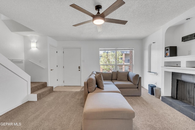 living area featuring ceiling fan, stairway, carpet, a textured ceiling, and a fireplace