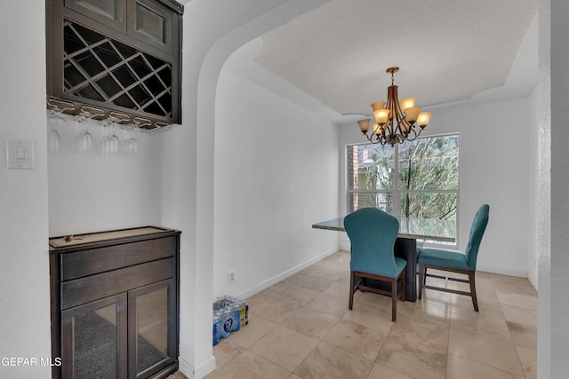 dining space featuring arched walkways, baseboards, a raised ceiling, a textured ceiling, and a notable chandelier