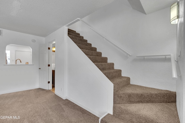 stairway with visible vents, carpet flooring, a textured ceiling, and baseboards