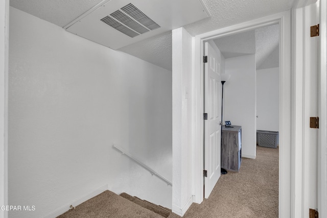 hallway featuring carpet floors, visible vents, and a textured ceiling