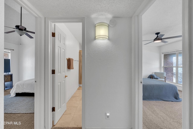 corridor featuring a textured ceiling, a textured wall, and light colored carpet