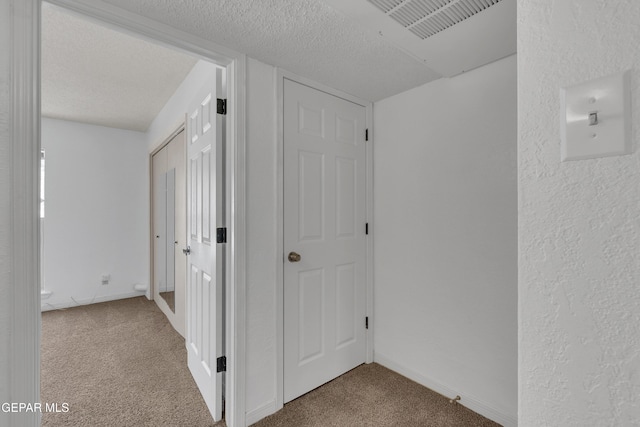 corridor featuring carpet, baseboards, a textured ceiling, and a textured wall