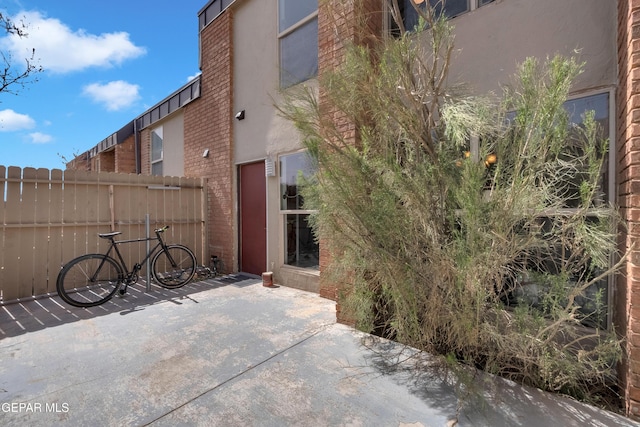 exterior space featuring brick siding, a patio, fence, and stucco siding