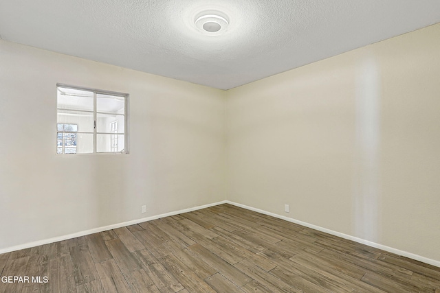 empty room featuring a textured ceiling, baseboards, and wood finished floors