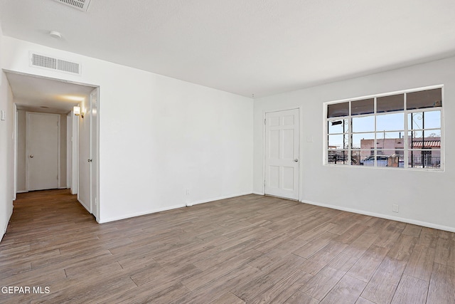 empty room featuring baseboards, visible vents, and wood finished floors