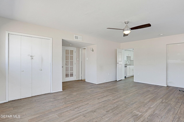 unfurnished bedroom featuring ceiling fan, light wood-style flooring, a sink, visible vents, and baseboards