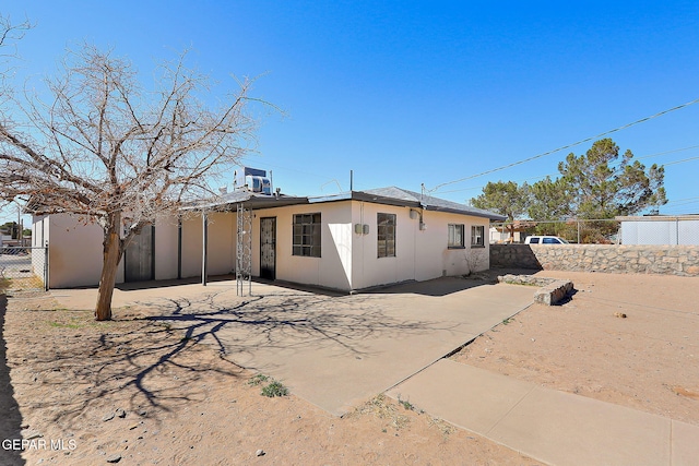 rear view of property featuring a patio area, fence, and stucco siding