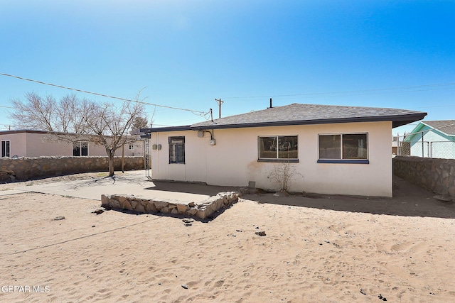 rear view of property with roof with shingles, fence, and stucco siding