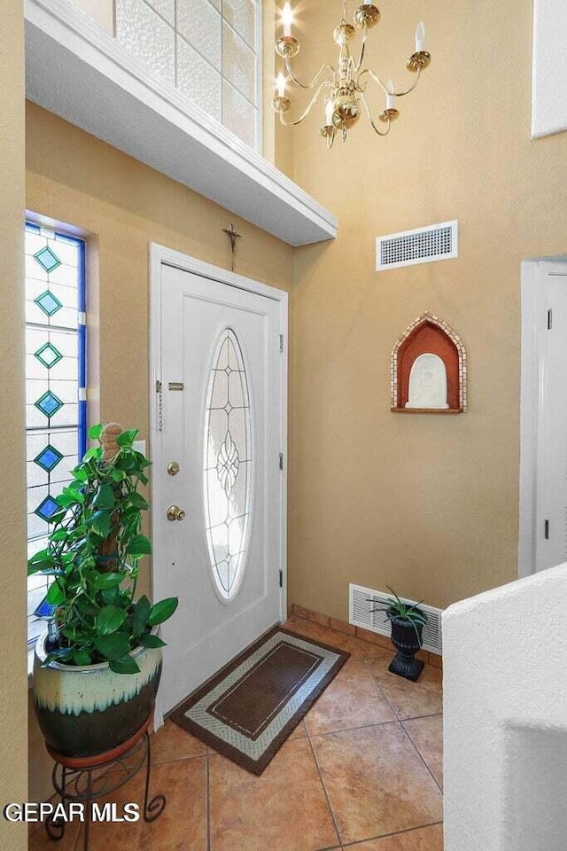 tiled foyer with a chandelier, a high ceiling, and visible vents