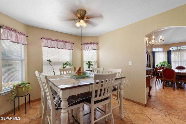 dining area with light tile patterned floors, baseboards, arched walkways, and ceiling fan with notable chandelier