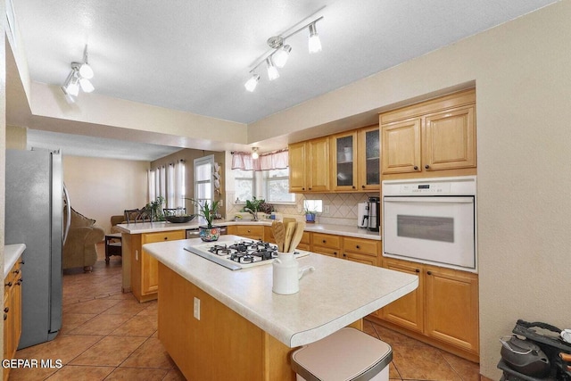 kitchen with white appliances, a center island, a peninsula, light countertops, and backsplash