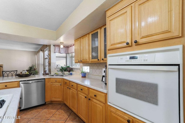 kitchen with light countertops, white appliances, backsplash, and a sink