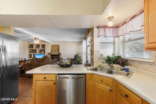 kitchen with a peninsula, a sink, open floor plan, light countertops, and appliances with stainless steel finishes