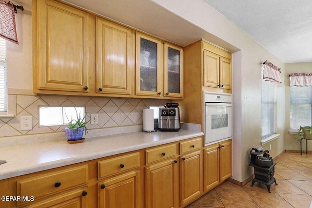 kitchen featuring light countertops, white oven, light tile patterned flooring, and decorative backsplash