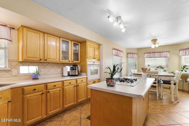 kitchen with tasteful backsplash, light countertops, light tile patterned flooring, a kitchen island, and white appliances