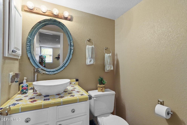 bathroom with toilet, a textured wall, a textured ceiling, and vanity