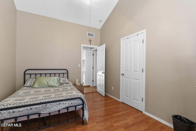 bedroom with high vaulted ceiling, wood finished floors, visible vents, and baseboards