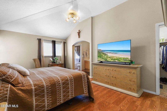 bedroom featuring arched walkways, wood finished floors, ensuite bathroom, an inviting chandelier, and vaulted ceiling