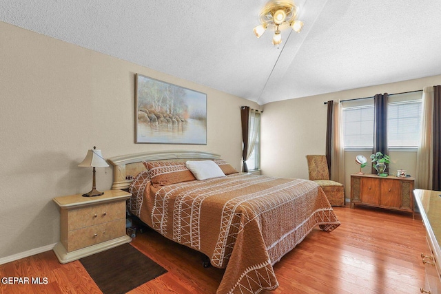 bedroom with lofted ceiling, a textured ceiling, baseboards, and wood finished floors