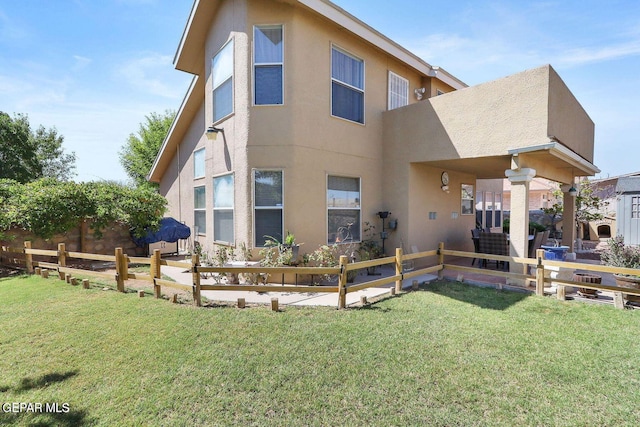 back of property with a lawn, fence, and stucco siding