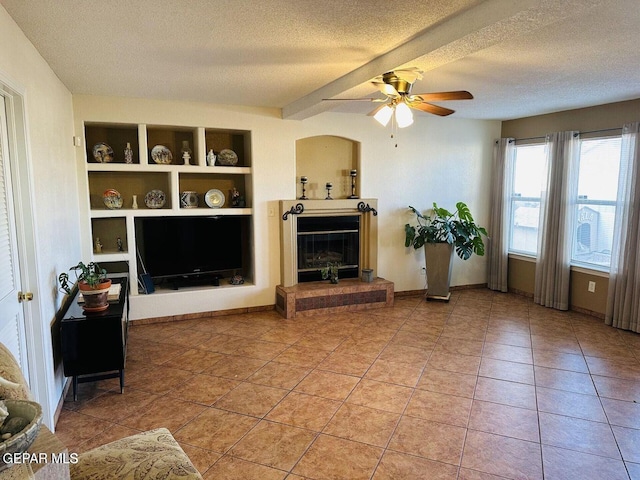 living area with a textured ceiling, ceiling fan, light tile patterned floors, built in features, and a glass covered fireplace