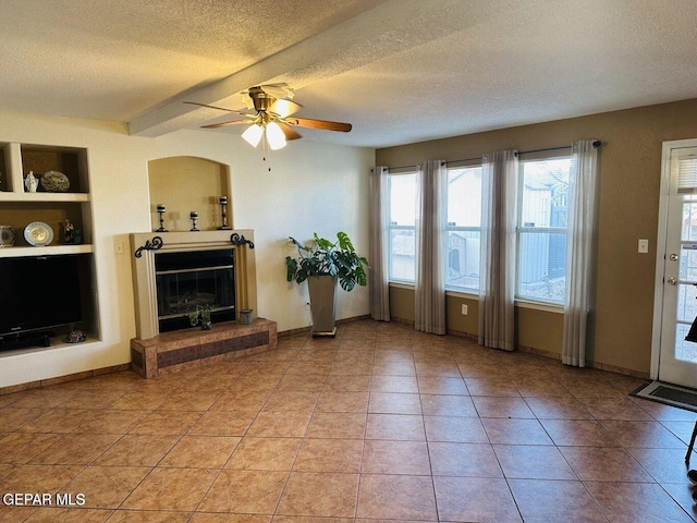 living room with built in features, a glass covered fireplace, a textured ceiling, and light tile patterned floors