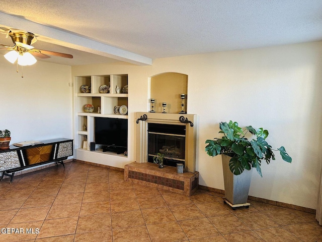 living room featuring baseboards, built in features, a glass covered fireplace, a textured ceiling, and light tile patterned flooring