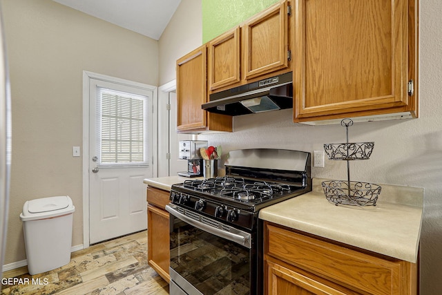 kitchen with light wood-style flooring, under cabinet range hood, light countertops, brown cabinetry, and gas stove