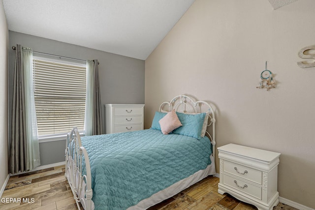 bedroom featuring light wood finished floors, baseboards, and vaulted ceiling