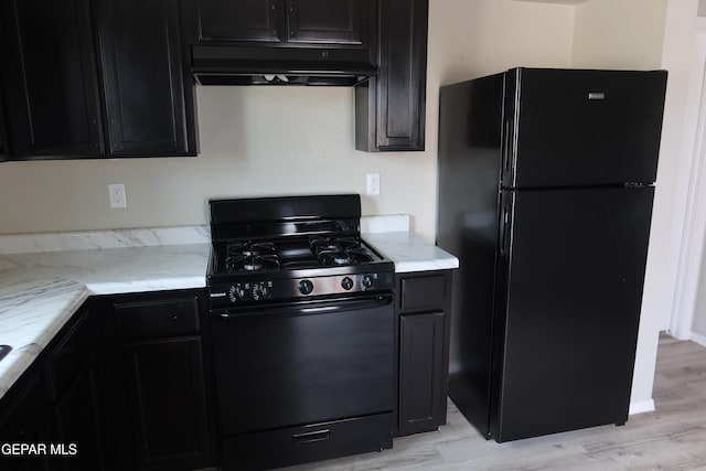 kitchen with light stone counters, dark cabinetry, under cabinet range hood, and black appliances