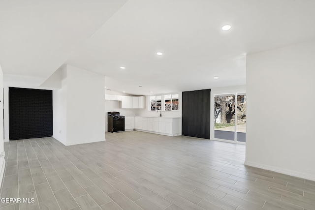 unfurnished living room with baseboards, recessed lighting, a sink, and wood tiled floor