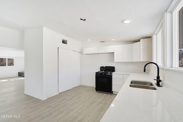 kitchen featuring light stone counters, light wood finished floors, white cabinets, black range with gas cooktop, and a sink