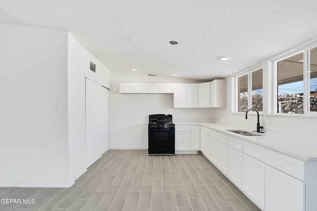 kitchen with light countertops, wood tiled floor, white cabinetry, black gas stove, and a sink