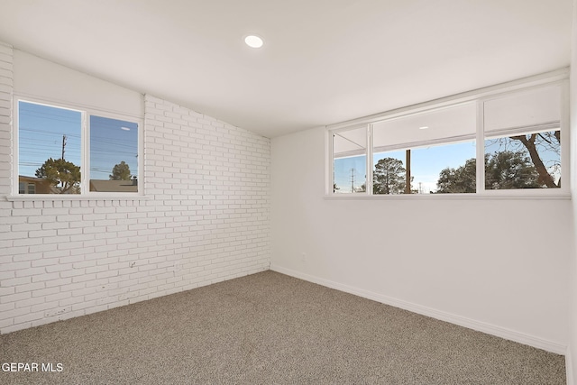 carpeted spare room featuring lofted ceiling and brick wall