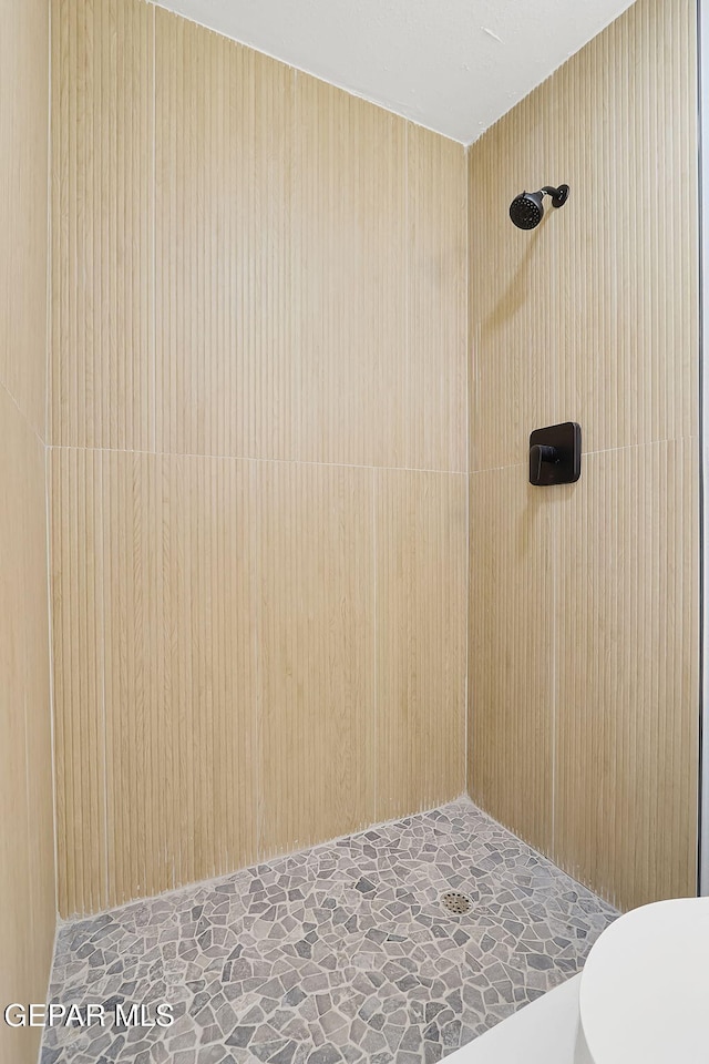 full bathroom featuring toilet, stone finish floor, and tiled shower