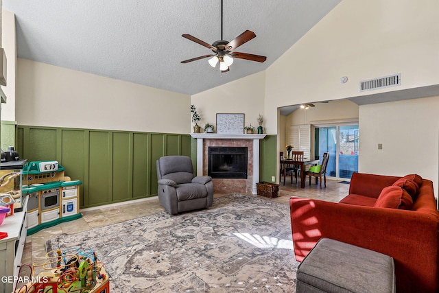 living area with visible vents, lofted ceiling, wainscoting, a fireplace, and a ceiling fan