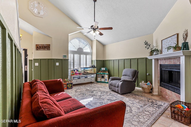 living room with tile patterned flooring, a wainscoted wall, a tile fireplace, a textured ceiling, and a ceiling fan