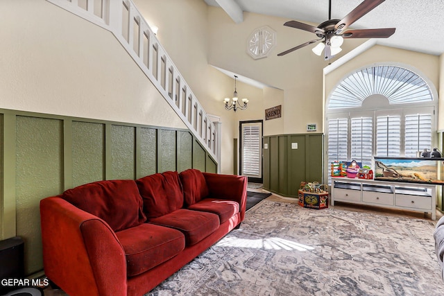 living area featuring stairway, a wainscoted wall, high vaulted ceiling, a decorative wall, and ceiling fan with notable chandelier