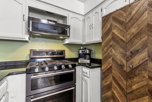 kitchen with white cabinetry, dark countertops, white dishwasher, and stainless steel gas range oven