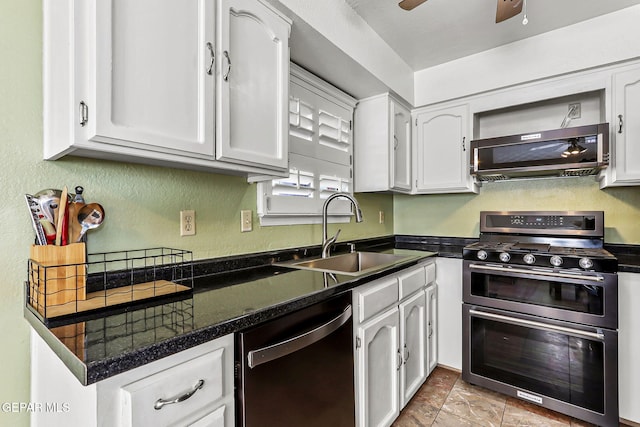 kitchen with dark countertops, a textured wall, white cabinets, stainless steel appliances, and a sink