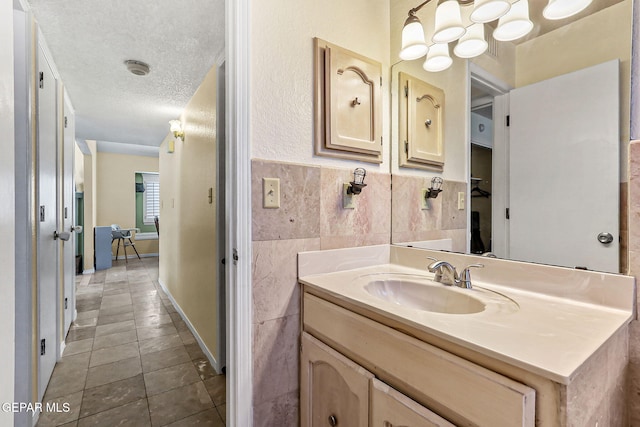 bathroom featuring vanity, a wainscoted wall, a textured ceiling, tile walls, and tile patterned floors