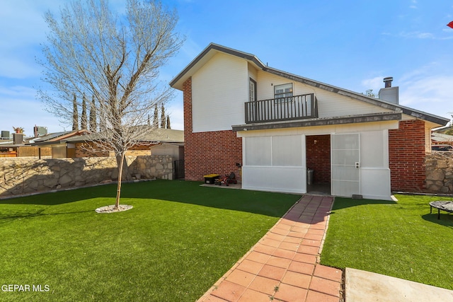 rear view of property featuring brick siding, a yard, a balcony, and fence