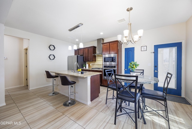 kitchen with backsplash, a kitchen bar, an island with sink, appliances with stainless steel finishes, and wall chimney exhaust hood