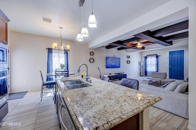 kitchen featuring visible vents, a kitchen island with sink, stainless steel appliances, a sink, and beamed ceiling