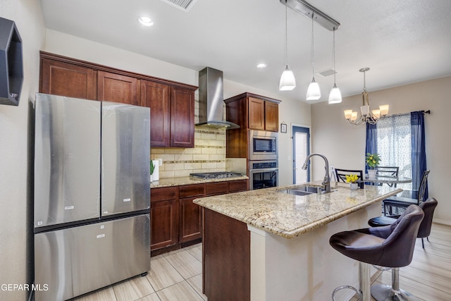 kitchen featuring light stone counters, a sink, decorative backsplash, stainless steel appliances, and wall chimney range hood