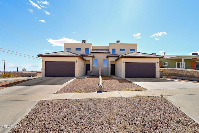 view of front of property featuring concrete driveway, a tiled roof, an attached garage, and stucco siding