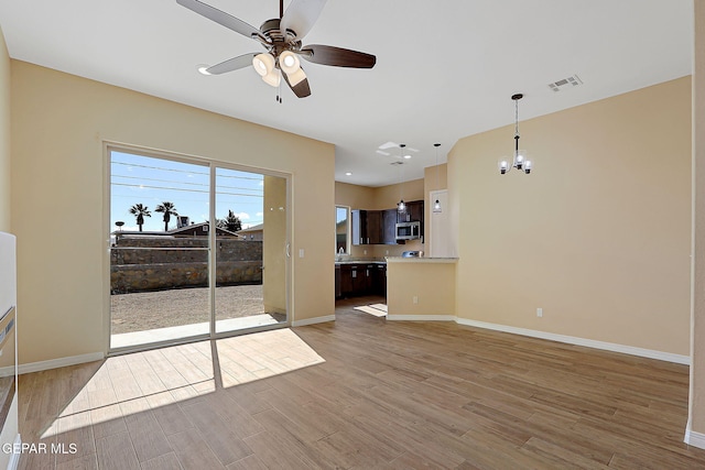 living area with ceiling fan with notable chandelier, light wood-style flooring, visible vents, and baseboards