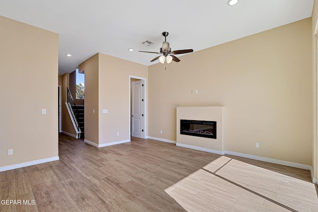 unfurnished living room with wood finished floors, stairway, a glass covered fireplace, and visible vents