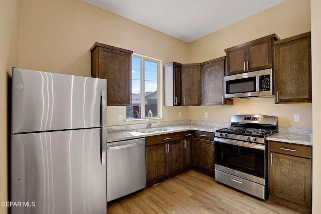 kitchen featuring dark brown cabinetry, light wood finished floors, light stone counters, appliances with stainless steel finishes, and a sink